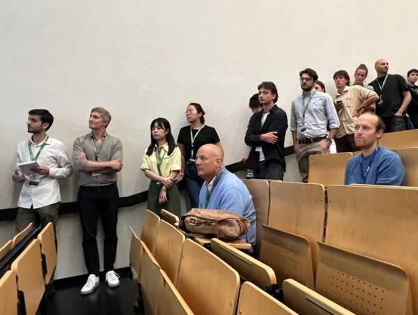 Young PhD students standing in line by the lecture hall wall