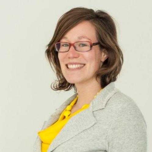 Portrait picture of a smiling caucasian woman wearing glasses, a light grey blazer and a yellow top